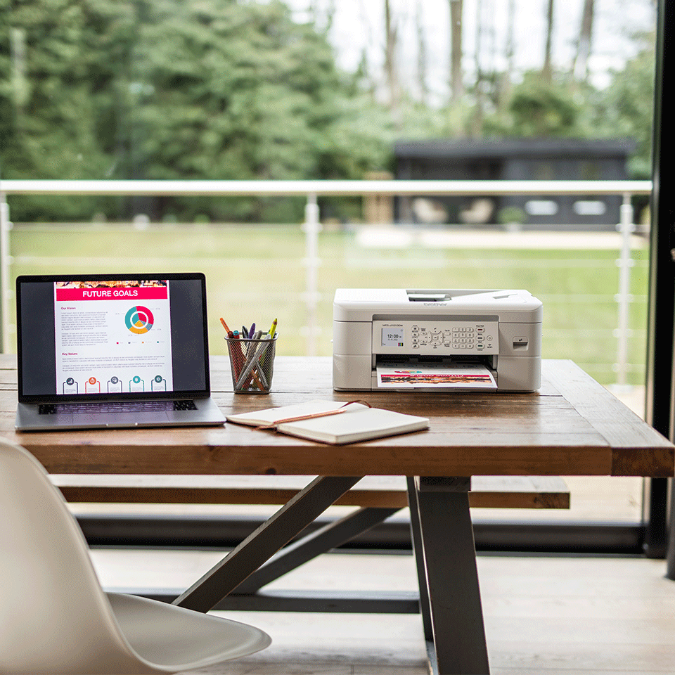 Brother MFC-J1010DW printer on a desk beside a laptop